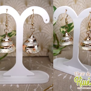 May include: Gold-toned earrings with a conical, layered design. The earrings have a metallic gold band around the base and are displayed on a white earring stand. The earrings are a unique accessory.