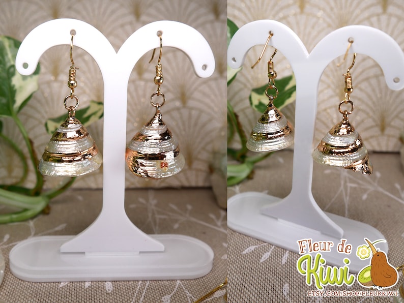 May include: Gold-toned earrings with a conical, layered design. The earrings have a metallic gold band around the base and are displayed on a white earring stand. The earrings are a unique accessory.