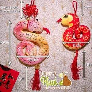Op de afbeelding: Twee pluche slangencharms met rode kwastjes. De slang links is roze en geel met een glinsterende afwerking. De slang rechts is rood met een bloemenpatroon. Beide slangen zijn ongeveer 10 cm lang. De charms zijn gelabeld met "Fleur de Kiwi" en "Etsy.com/shop/fleurkiwi".