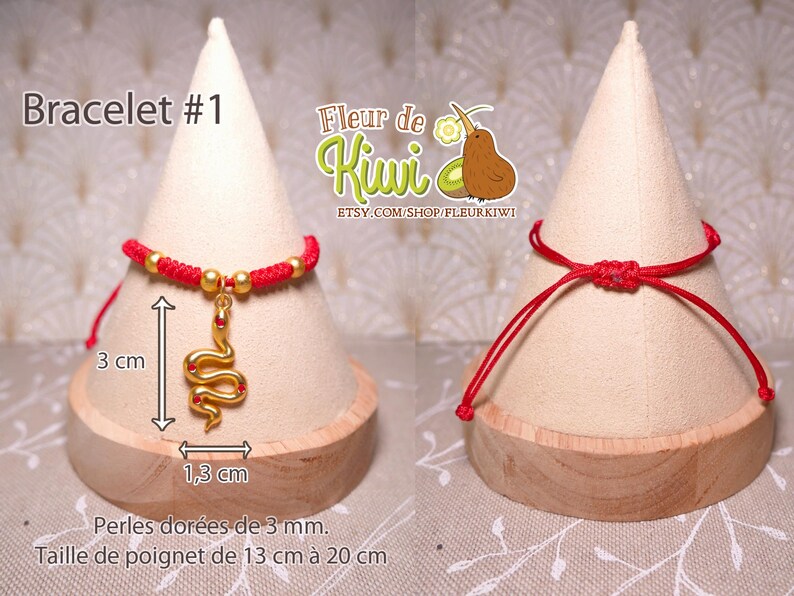 Op de afbeelding: Rood koord armband met een gouden slang bedel. Het armband is 3 cm lang en de bedel is 1,3 cm lang. Het armband is gemaakt met 3 mm gouden kralen. Het armband wordt getoond op een houten display stand.