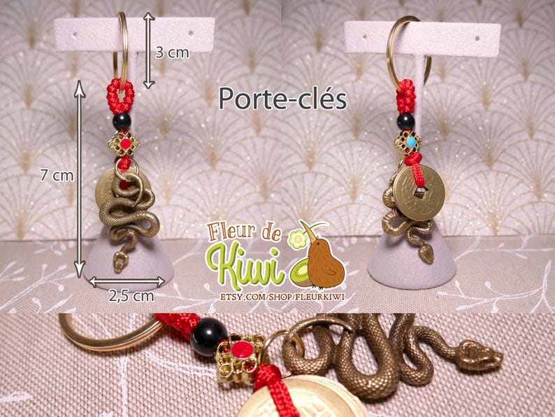 Op de afbeelding: Een gouden slangenhanger met een munt en rode kralen hangt aan een gouden sleutelhanger. De hanger is bevestigd aan een grijze basis en is 7 cm lang. De hanger is 2,5 cm breed. De hanger is 3 cm hoog. De hanger is een slang met een munt op zijn kop. De munt heeft een Chinees karakter erop. De hanger is een sleutelhanger.