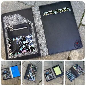 May include: Black faux leather portfolio with a decorative marbled pattern and a clear pocket with colorful confetti. The portfolio has a zippered pocket, a pen holder, and a logo in the bottom right corner. The portfolio is open, revealing the interior.