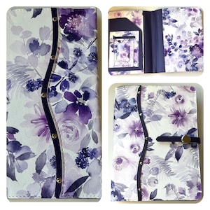 May include: A white and purple floral patterned journal cover with a dark blue spine and snap closure. The cover features a watercolor design of purple flowers and foliage. The journal is shown closed, open, and with an interior pocket.
