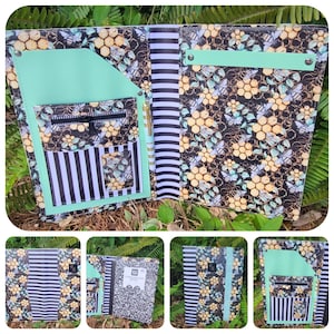 May include: A black and white striped notebook cover with a bee and honeycomb pattern. The cover has a mint green pocket and accents, with a zippered pocket and pen holder. The notebook is open, revealing a black and white striped spine.