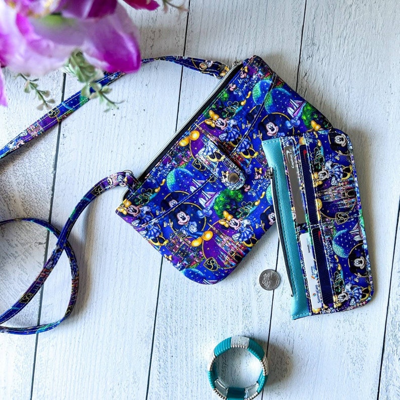 May include: A blue and purple crossbody purse with a Disney character print. The purse has a zippered pocket and a snap closure. The purse is paired with a matching blue and purple wallet with multiple card slots.