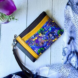 Pode incluir: Uma bolsa com z&iacute;per preta e amarela com um forro de tecido azul e roxo com uma estampa de Mickey Mouse e Minnie Mouse. A estampa inclui um castelo, fogos de artif&iacute;cio e outras imagens com tema Disney.