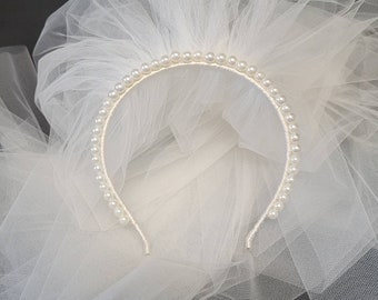 May include: A white tulle veil with a pearl headband. The headband is made of a thin metal band with a row of white pearls.