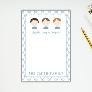 May include: A personalized notepad featuring three cartoon figures with different hair colors. The notepad has a light blue bow-tie pattern border and includes the text "Brock, Trey & Cooper" and "THE SMITH FAMILY". A pencil and paper clip are visible.