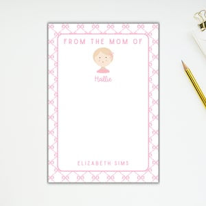 May include: Pink notepad with a pink and white checkered border. The notepad has a pink illustration of a girl with a flower in her hair. The text "FROM THE MOM OF" is at the top of the notepad. The text "Hallie" is below the illustration. The text "ELIZABETH SIMS" is at the bottom of the notepad.
