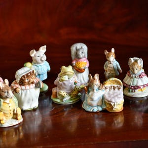Może przedstawiać: Kolekcja dziesięciu małych ceramicznych figurek zwierząt przedstawiających antropomorficzne postacie w ubraniach, w tym króliki, świnię, żabę, wiewiórkę i myszy, z których każda jest pomalowana w różne kolory z wyraźnymi detalami twarzy.