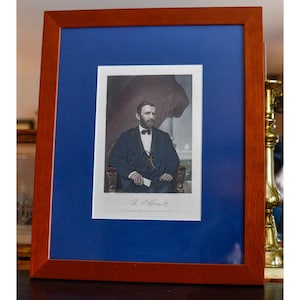 May include: Framed portrait of a man in a dark suit and bow tie, seated in a chair. The portrait is set against a blue background within a wooden frame. The image is a historical print.