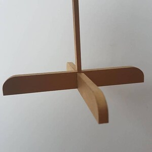 Op de afbeelding: Een houten standaard met vier poten en een verticale steun. De standaard is gemaakt van lichtbruin hout en heeft een eenvoudig ontwerp.