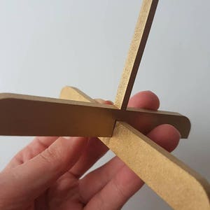 Op de afbeelding: Een gouden houten standaard met vier poten die een X vormen. De standaard is gemaakt van dunne, platte stukken hout.