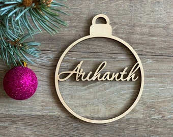 May include: A wooden Christmas ornament shaped like a bauble with the name "Arihanth" cut out in the center.