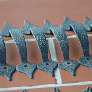 May include: A row of 10 black metal door handles with a decorative, textured finish. The handles are arranged in a line on a brick surface.