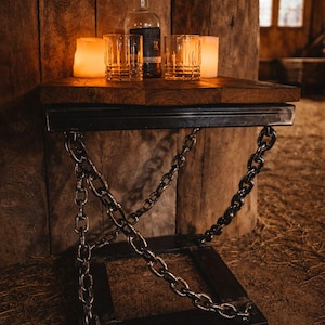 May include: A side table with a dark wood surface, suspended by chains and a black metal frame. It features a bottle of liquor, two glasses, and two candles. The scene is set in a dimly lit, wooden interior, evoking a rustic feel.