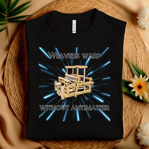 Peut inclure: T-shirt noir avec un motif de métier à tisser en bois et des rayons lumineux bleus. Le texte "WEAVERS WARP" est au-dessus du métier à tisser et "WITHOUT ANTIMATTER" en dessous. Le t-shirt est en matière souple.