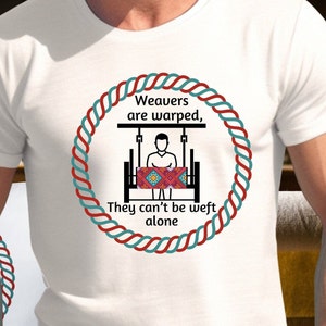 May include: White t-shirt with a red and blue rope design around a graphic of a person weaving on a loom. The text reads "Weavers are warped, They can't be weft alone."