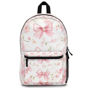 May include: White backpack with a pink bow and floral pattern. The backpack has a black zipper, handle, and mesh side pocket. The design features pink bows and flowers on a white background.