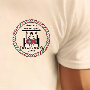 May include: White t-shirt with a red, white, and blue circular design featuring a person weaving on a loom. The text reads "Weavers are warped, They can't be weft alone."