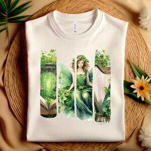 May include: A white t-shirt with a green fairy design. The fairy is sitting on a harp and surrounded by green leaves. The design is in a watercolor style.
