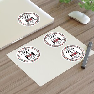 May include: White stickers with a red, white, and green rope border. The stickers feature the text "Weavers are warped, they can't be weft alone" around a graphic of a person on a loom. One sticker is on a laptop.