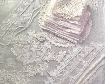 May include: An assortment of white lace and fabric pieces, including doilies, ribbons, and floral appliqués, arranged on a white surface. Various lace trims and embellishments are visible, showcasing different patterns and textures. The collection appears to be for crafting or sewing projects.