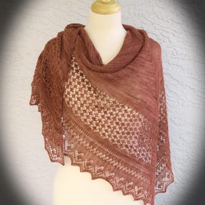 May include: A rust-colored triangular shawl featuring a combination of solid stockinette stitch sections and intricate openwork lace panels. The edges of the shawl display a delicate scalloped border pattern, crafted with fine yarn in a warm earth tone.