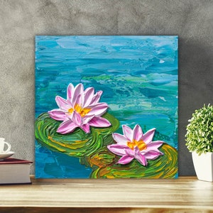 May include: A painting of two pink water lilies with yellow centers, floating on green lily pads in a blue pond. The painting is done in a textured style, giving the impression of brushstrokes.
