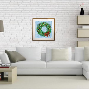 May include: A framed print of a Christmas wreath with a red bow. The wreath features green leaves, red berries, and festive decorations, set against a light blue backdrop. The artwork is displayed on a white brick wall.
