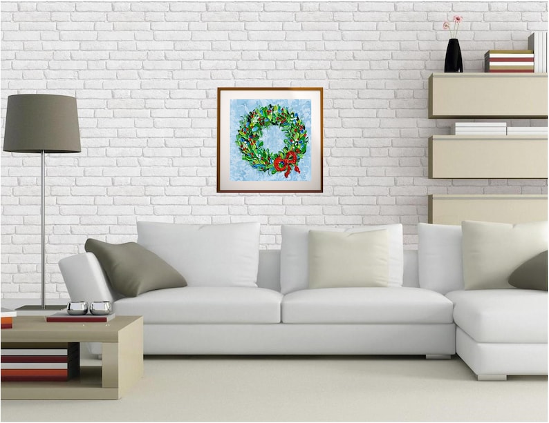 May include: A framed print of a Christmas wreath with a red bow. The wreath features green leaves, red berries, and festive decorations, set against a light blue backdrop. The artwork is displayed on a white brick wall.