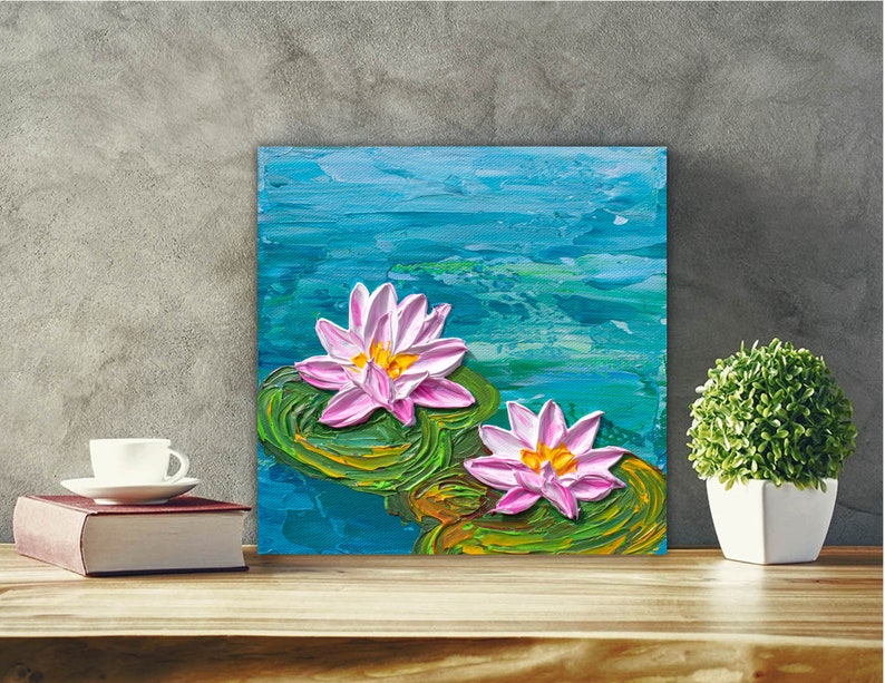 May include: A painting of two pink water lilies with yellow centers, floating on green lily pads in a blue pond. The painting is done in a textured style, giving the impression of brushstrokes.