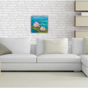 May include: A white sectional sofa with two pillows and a painting of pink water lilies on a blue background hanging on a white brick wall.