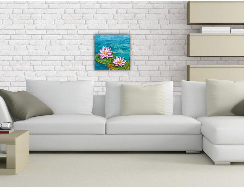 May include: A white sectional sofa with two pillows and a painting of pink water lilies on a blue background hanging on a white brick wall.