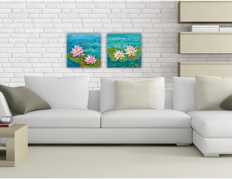 May include: Two framed paintings of water lilies on a white brick wall above a white sectional sofa with gray throw pillows.