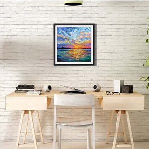 May include: A framed landscape painting depicts a vibrant sunset over water. The artwork features bold brushstrokes of orange, yellow, blue, and purple, creating a textured and colorful scene. The painting is displayed on a white brick wall.
