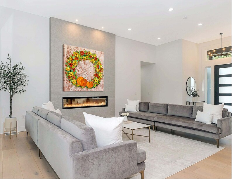May include: A modern living room with a gray sectional sofa, a fireplace, and a large wall art piece featuring a wreath of fall leaves and pumpkins.