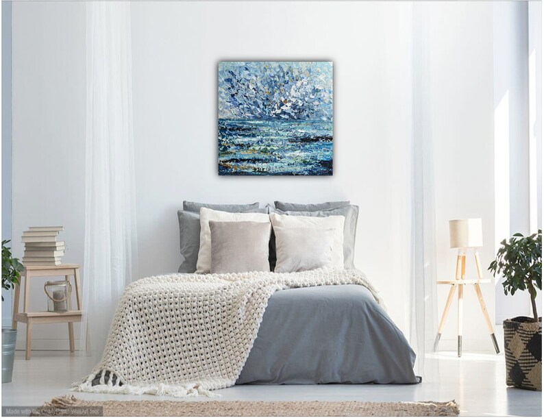 K&ouml;nnte beinhalten: Abstraktes Gem&auml;lde einer Meereslandschaft in Blau-, Wei&szlig;- und Goldt&ouml;nen mit strukturiertem, pastosem Finish. Das Kunstwerk h&auml;ngt &uuml;ber einem Bett mit einer grauen Bettdecke und einer cremefarbenen Strickdecke. Es erinnert an Meer und Himmel.