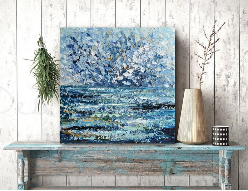 K&ouml;nnte beinhalten: Quadratisches abstraktes Gem&auml;lde mit Meereslandschaft. Das Kunstwerk zeigt strukturierte Pinselstriche in Blau-, Wei&szlig;- und Goldt&ouml;nen, die Wellen und einen bew&ouml;lkten Himmel darstellen. Das Gem&auml;lde wird auf einem blau-verwitterten Holzregal pr&auml;sentiert.