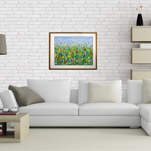 Puede incluir: Una pintura enmarcada que representa un campo vibrante de flores coloridas bajo un cielo azul. La obra de arte presenta una variedad de flores en tonos de rojo, amarillo, azul y verde. La pintura se exhibe en una pared de ladrillo blanco sobre un sof&aacute; blanco.