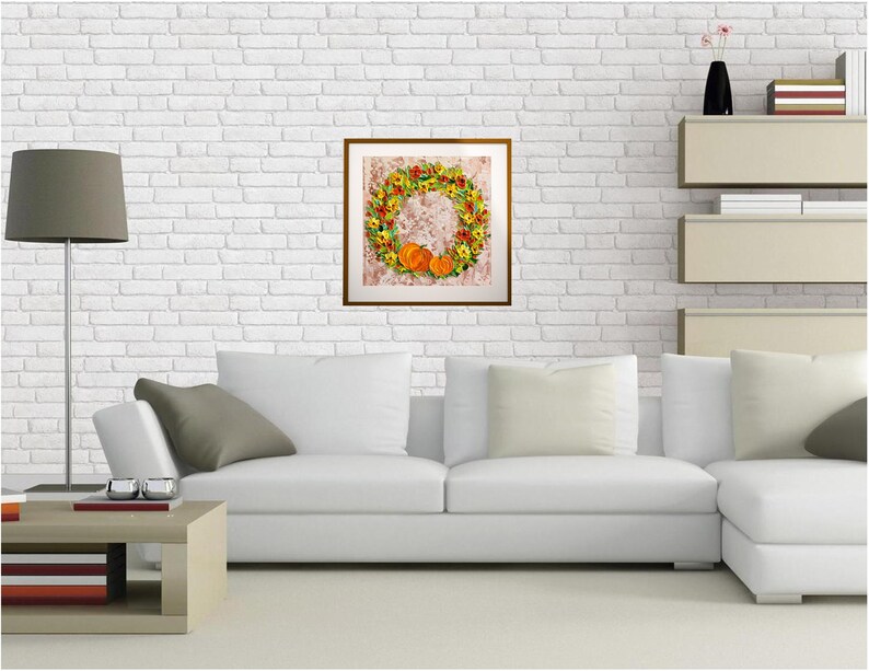 May include: A white couch with gray pillows in a living room setting. A framed picture of a fall wreath with pumpkins hangs on a white brick wall.