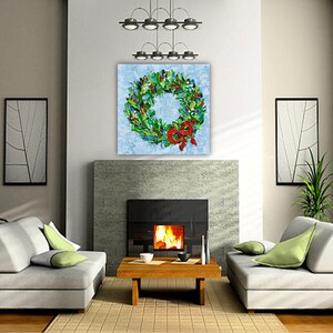 May include: A vibrant Christmas wreath artwork featuring green foliage, red berries, and a red bow. The painting is displayed above a fireplace in a contemporary living room. The room includes grey sofas, a wooden coffee table, and framed wall art.