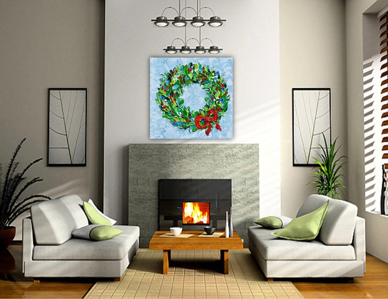 May include: A vibrant Christmas wreath artwork featuring green foliage, red berries, and a red bow. The painting is displayed above a fireplace in a contemporary living room. The room includes grey sofas, a wooden coffee table, and framed wall art.