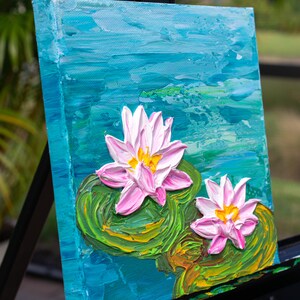 May include: A painting of two pink water lilies with yellow centers on a blue and green background. The lilies are painted in a textured style, giving the impression of brushstrokes.