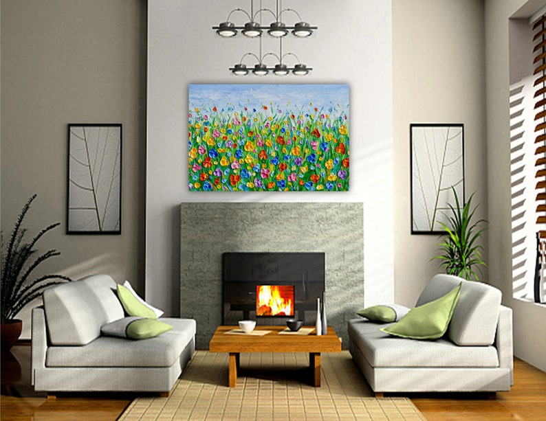 Puede incluir: Una vibrante pintura floral con un cielo azul de fondo cuelga sobre una chimenea. La obra de arte presenta flores coloridas en tonos de rojo, amarillo, azul y verde. La habitaci&oacute;n incluye dos sof&aacute;s grises, una mesa de centro de madera y plantas decorativas.
