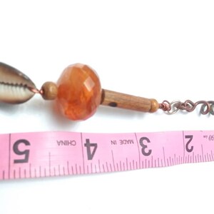 May include: A brown seashell, an orange glass bead, a wooden bead, and a copper wire chain are strung together. The chain is coiled at the end. A pink measuring tape with the numbers 1, 2, 3, 4, and 5 is visible in the background. "#09" is printed on the tape.
