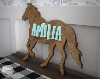 May include: Wooden horse silhouette with the name "AMILIA" spelled out in light blue letters.