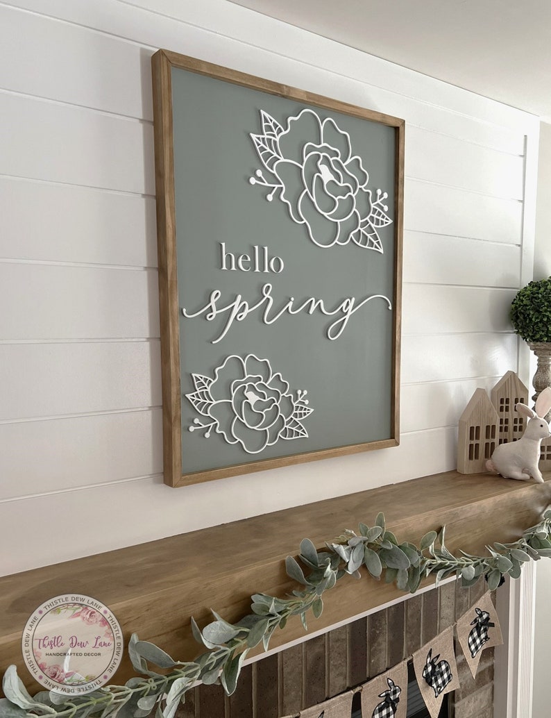 May include: A gray wooden sign with a white wooden cutout of flowers and the text "hello spring".
