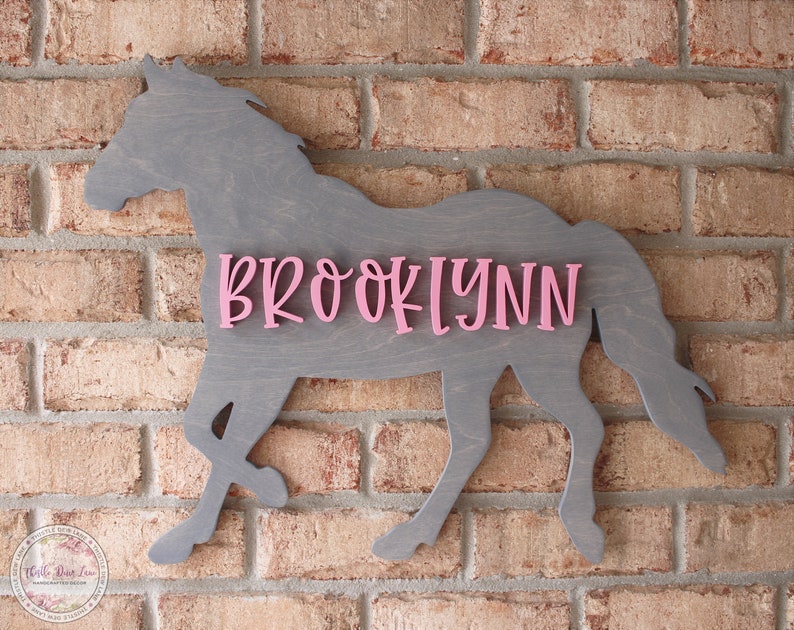 May include: A gray wooden horse silhouette with the name "BROOKLYNN" in pink letters.
