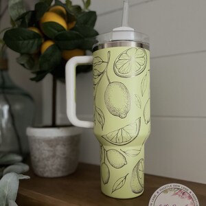 Pu&ograve; includere: Un bicchiere in acciaio inossidabile verde chiaro con un design di limone bianco e nero. Il bicchiere ha un coperchio e un manico. Il bicchiere &egrave; appoggiato su una superficie di legno. Il testo sull'adesivo recita "Thistle Dew Lane Handmade Decor".